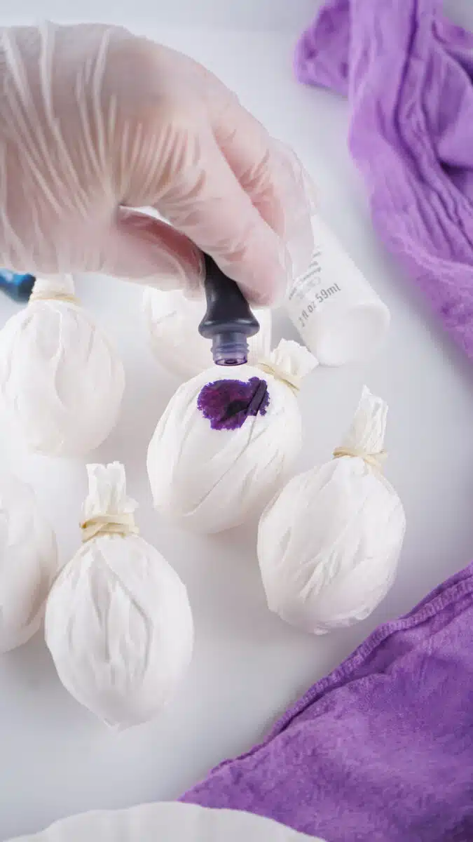 Dyeing fabric-wrapped objects with purple dye for a galaxy Easter egg craft project.