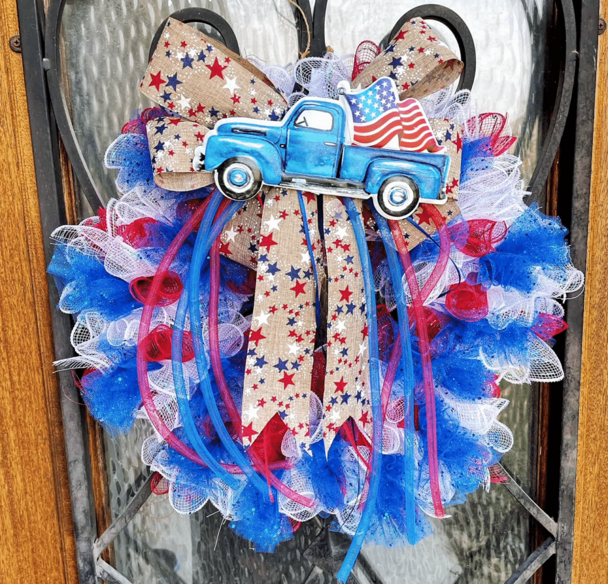 Fourth of July wreaths, showcasing red, white, and blue colors, stars, and a central vintage truck motif, displayed on a door.