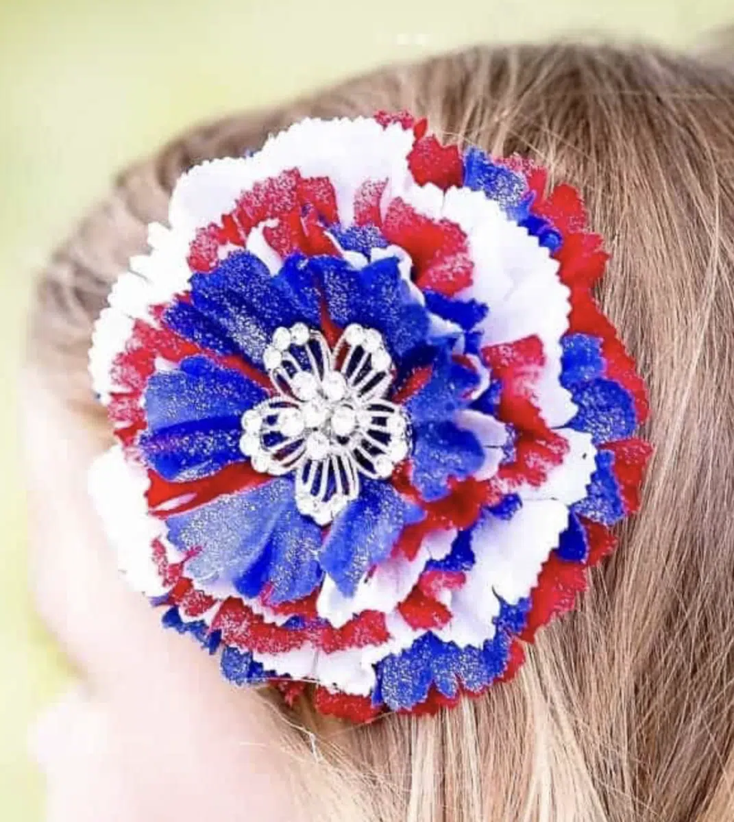 A red, white, and blue artificial flower hair accessory, perfect for Fourth of July crafts, attached to a person's hair.