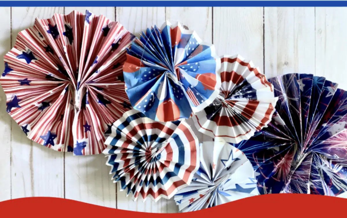 Paper fans with patriotic colors for Fourth of July displayed on a wooden surface.