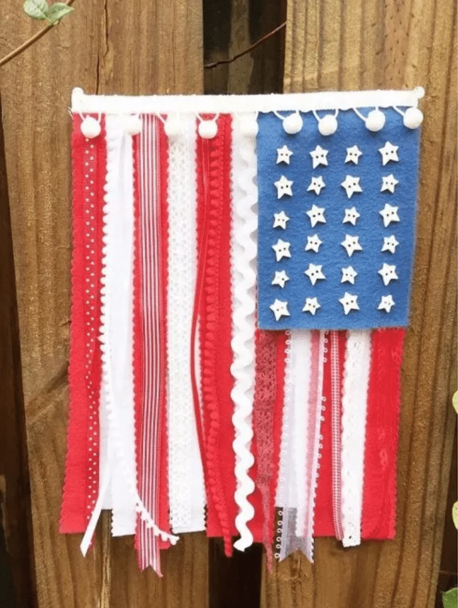 A handmade Fourth of July-inspired wall decoration with red, white, and blue ribbons and white stars attached to a blue fabric square.