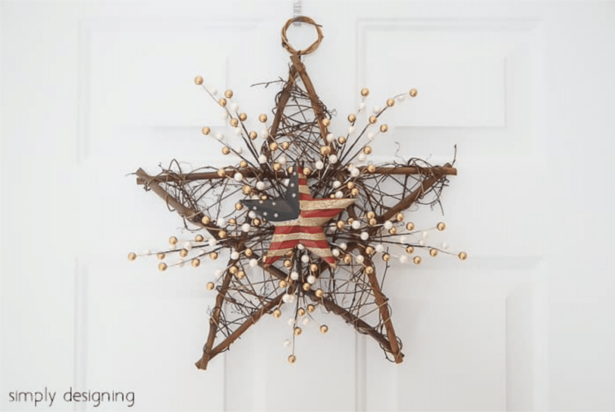 A Fourth of July rustic-style star-shaped wreath with berry accents and a central American flag motif hangs on a white door.