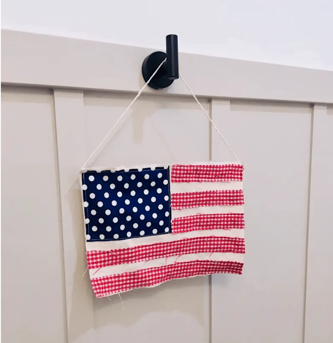 An American flag-themed fabric wall hanging on a hook, perfect for Fourth of July crafts.