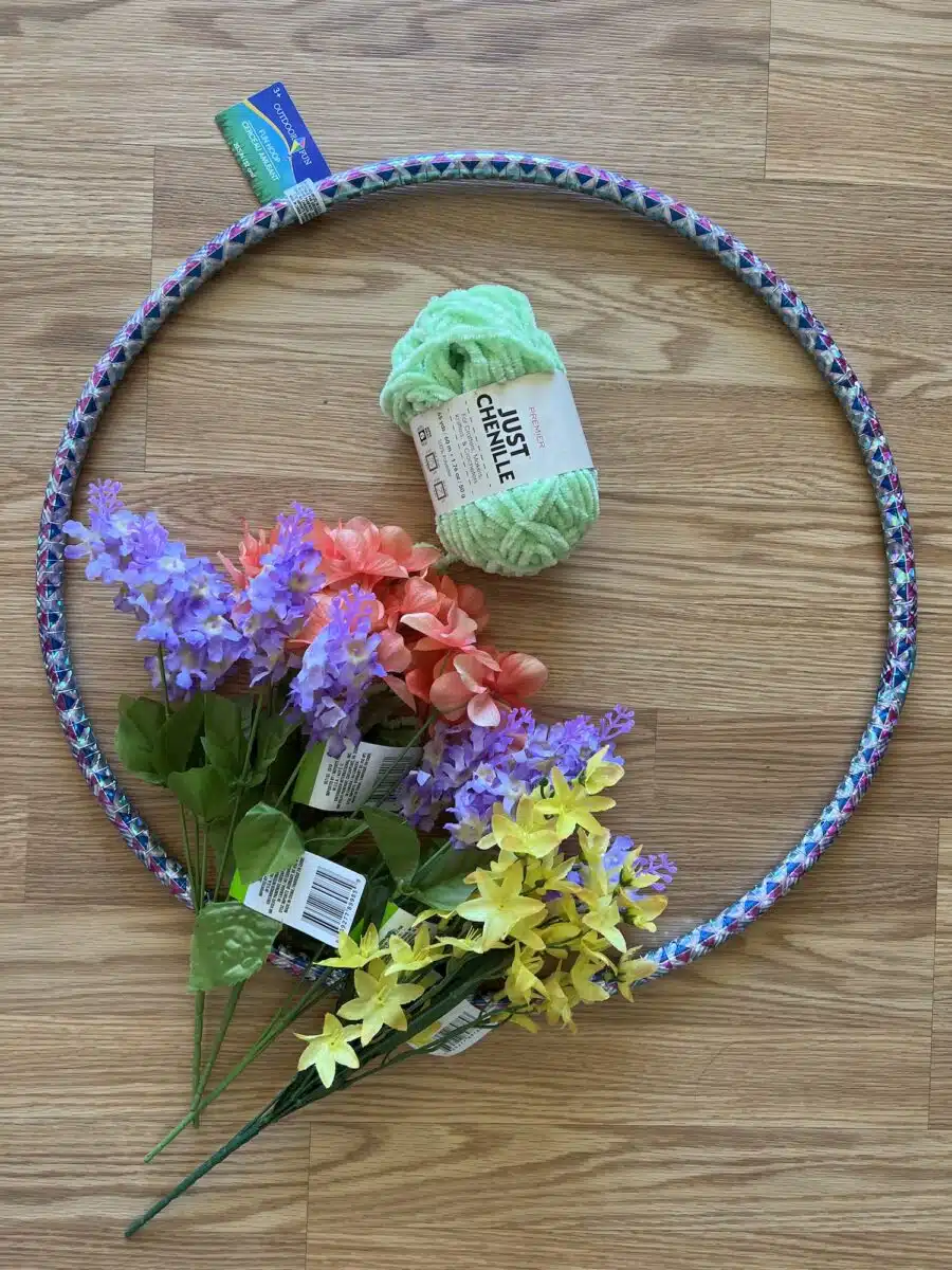 A hula hoop, a bundle of green yarn, and assorted artificial flowers on a wooden floor.
