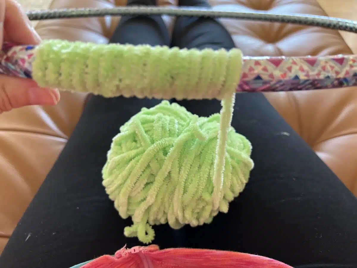 Person sitting with a hula hoop and a green fuzzy pom-pom against their legs.
