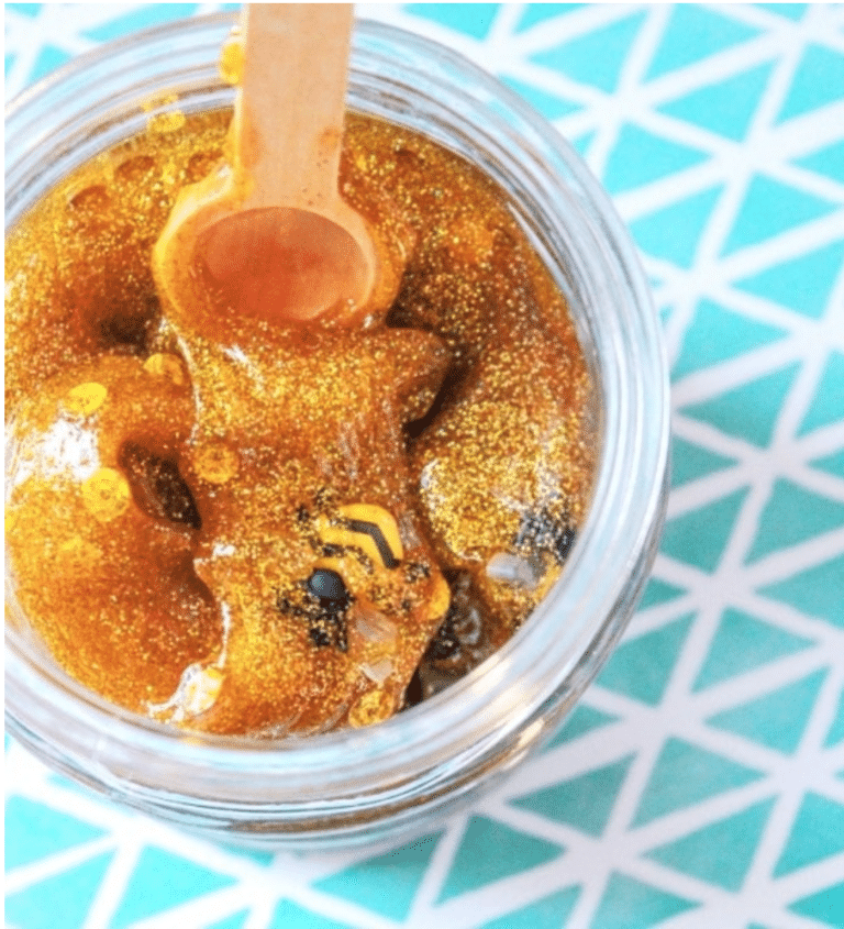 clear jar with honey colored slime with glitter and bumble bees inside against blue and white table