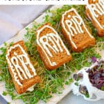 A plate of Halloween-themed tombstone sandwiches shaped like tombstones, with "RIP" written in icing, placed on a bed of greens. A skull decoration sits nearby on the right.