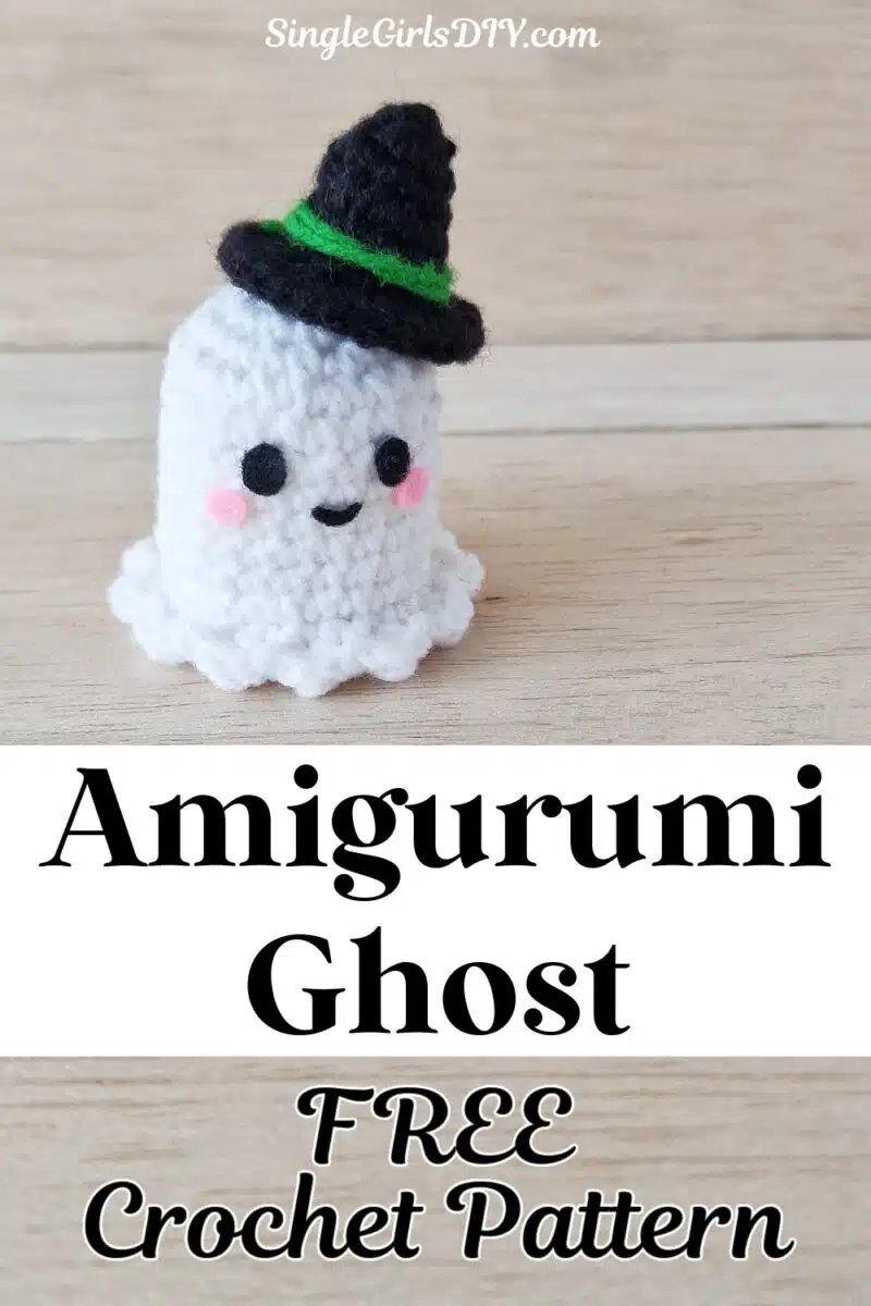 A small crocheted amigurumi ghost with a black hat rests on a wooden surface. Text above and below the ghost reads, "Amigurumi Ghost FREE Crochet Pattern." Website name at the top.