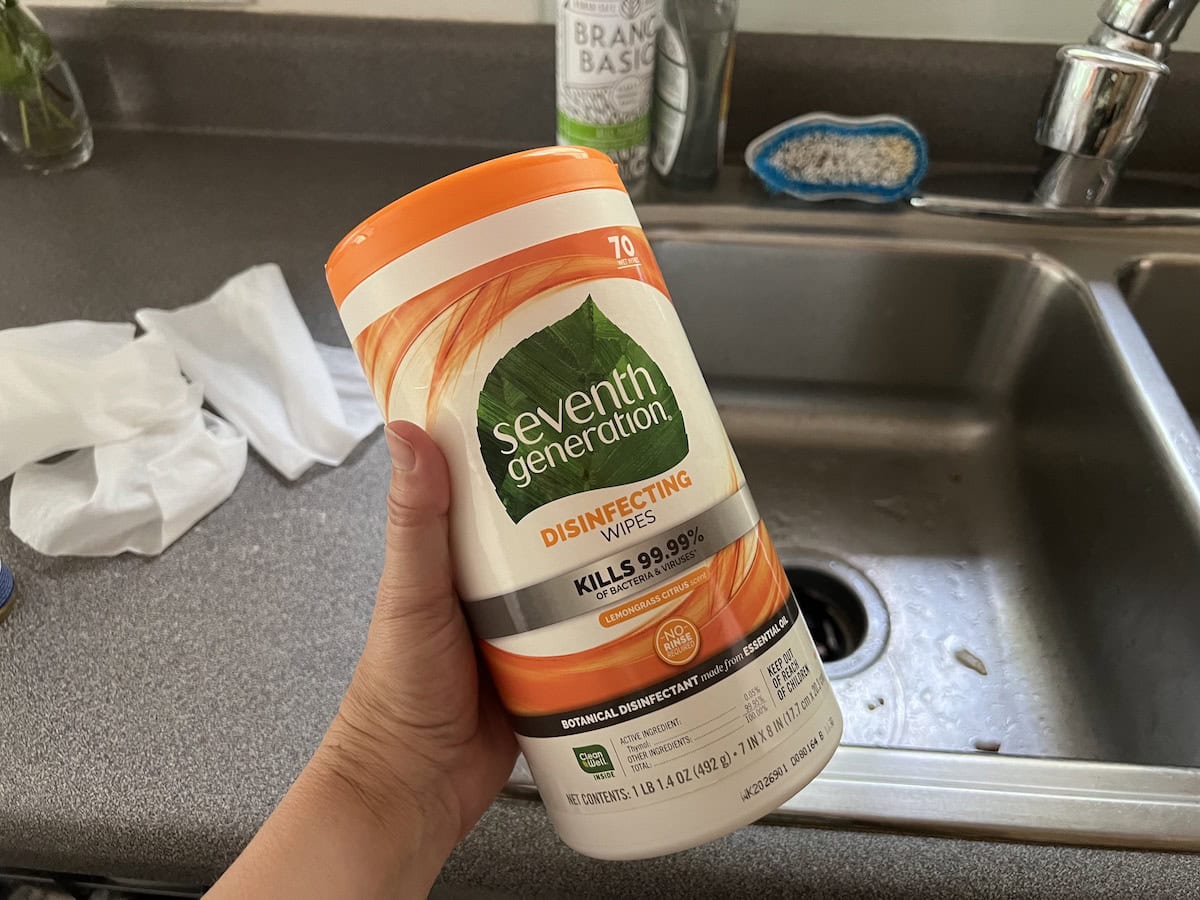 Hand holding a container of Seventh Generation disinfecting wipes above a kitchen sink.