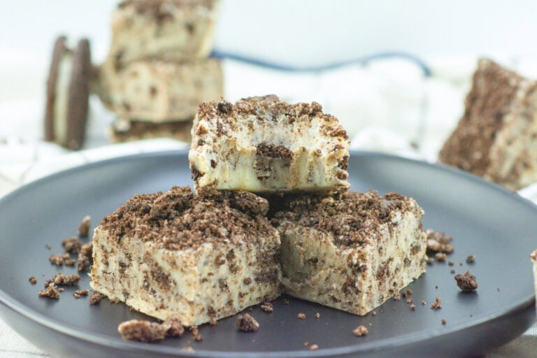 Three cookies and cream fudge squares on a black plate, with crumbled cookies on top and around them.