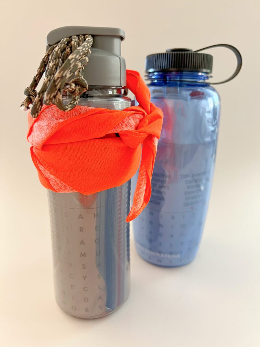 Two water bottles: a silver one with a red bandana and a keychain, and a blue one with a black cap.