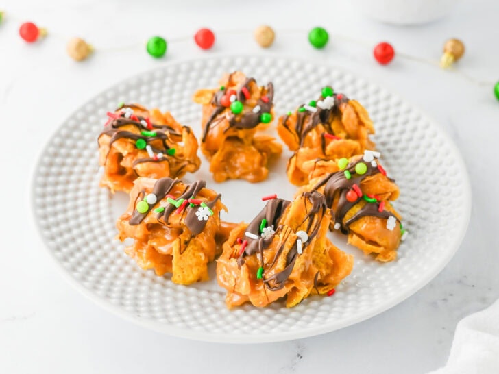 A white plate with five festive cookies drizzled with chocolate and topped with colorful sprinkles.