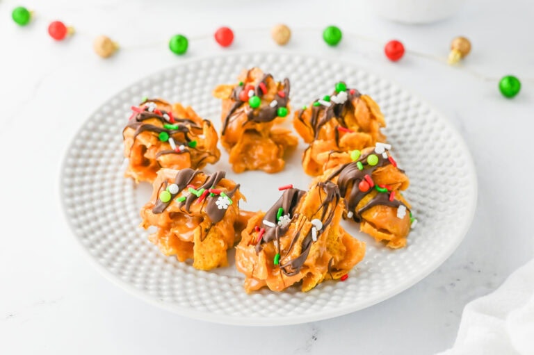 A white plate with five festive cookies drizzled with chocolate and topped with colorful sprinkles.