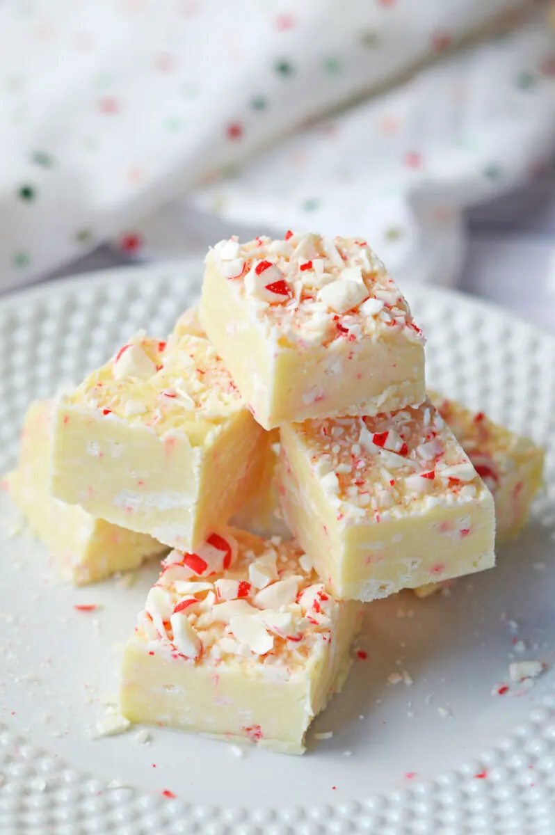 A stack of white chocolate peppermint fudge squares on a white plate, topped with crushed peppermint candy.