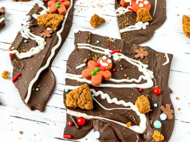 Chocolate bark with gingerbread decorations and sprinkles on a white wooden surface.