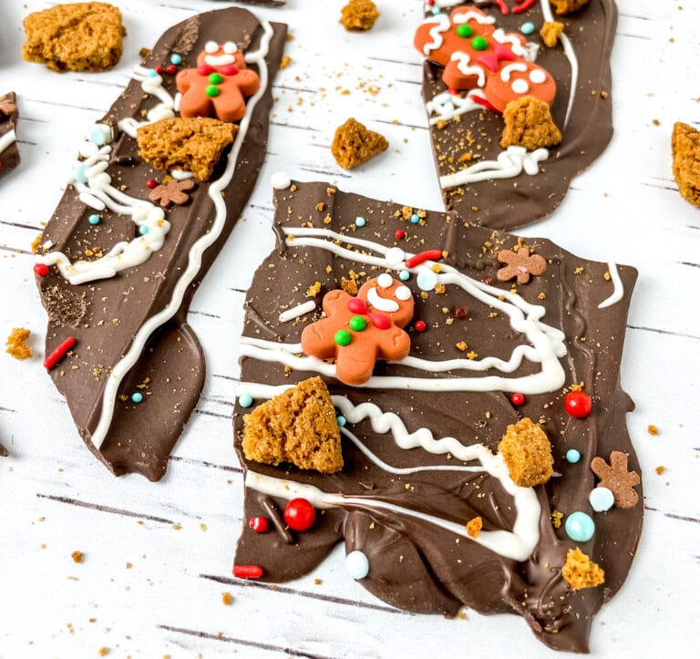 Chocolate bark with gingerbread decorations and sprinkles on a white wooden surface.