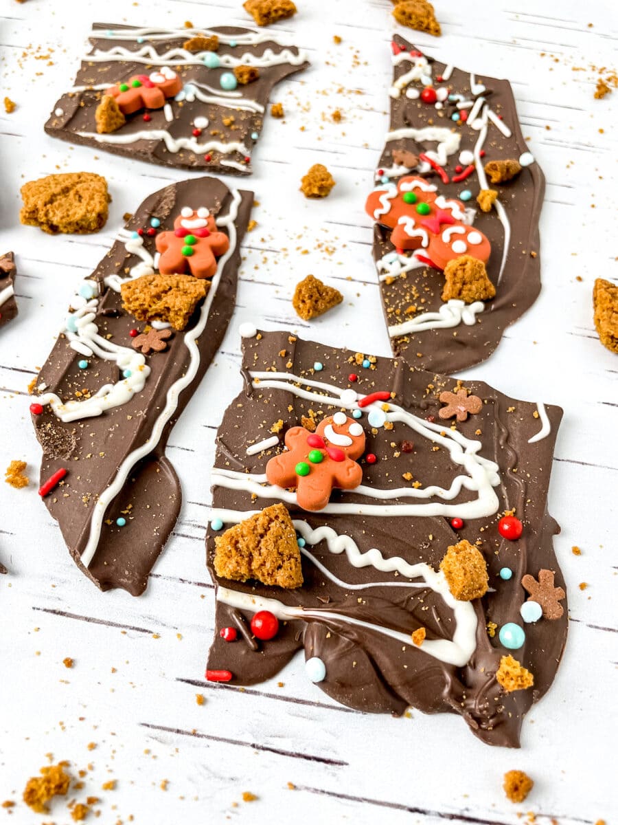 Chocolate bark with gingerbread cookie pieces, sprinkles, and white chocolate drizzle on a white surface.