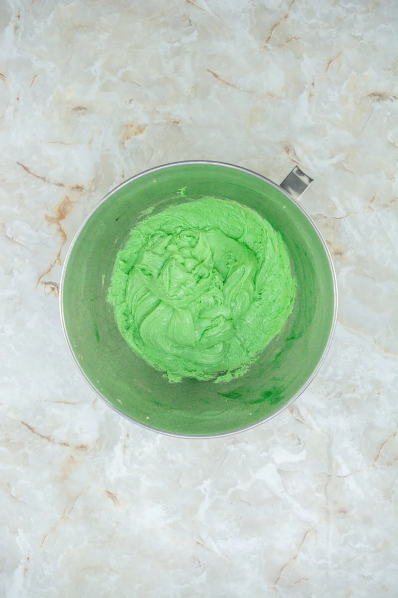 A metal bowl filled with bright green frosting sits on a marble surface.