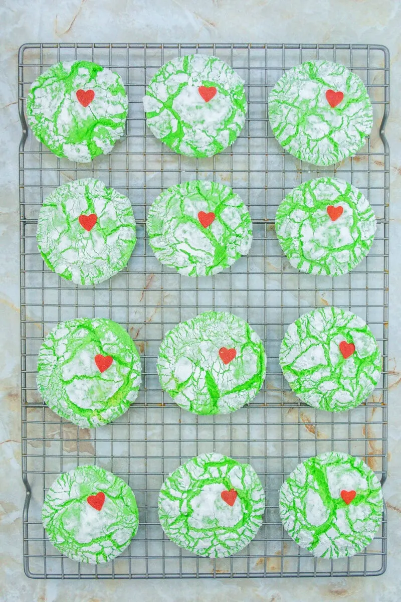 Twelve green crinkle cookies with red heart decorations on a cooling rack.