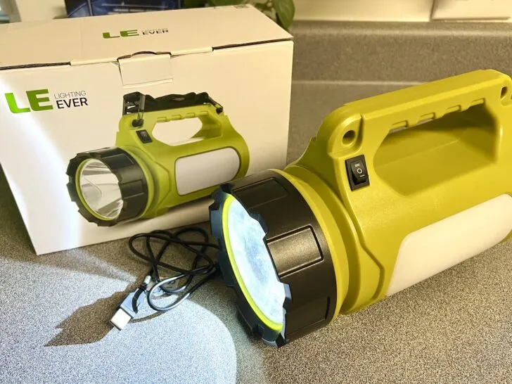 A green LED flashlight with a black handle is on a counter next to its box. A USB charging cable is also visible.