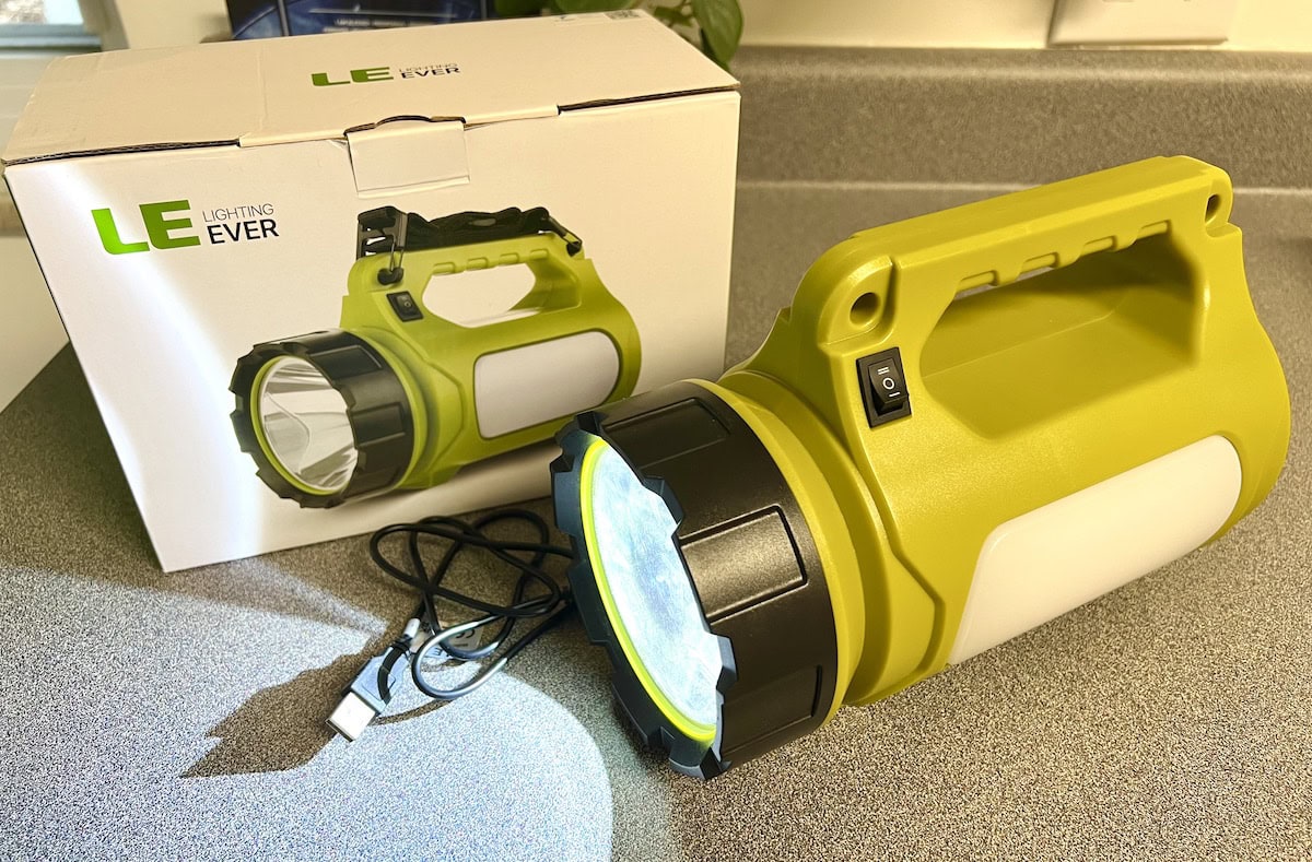 A green LED flashlight with a black handle is on a counter next to its box. A USB charging cable is also visible.