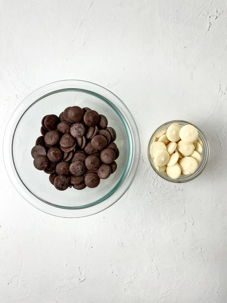 Two glass bowls on a white surface: the left bowl contains dark chocolate wafers, and the right bowl contains white chocolate wafers.