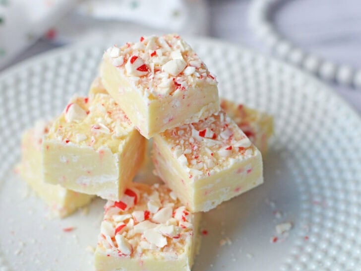 A stack of white chocolate fudge pieces topped with crushed peppermint is displayed on a white plate.