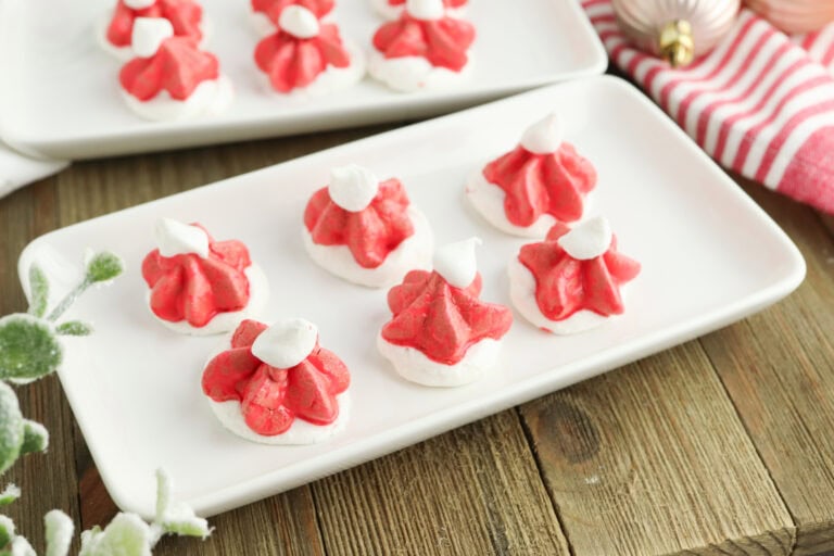 Red and white meringue cookies shaped like Santa hats on a rectangular white plate, placed on a wooden table.