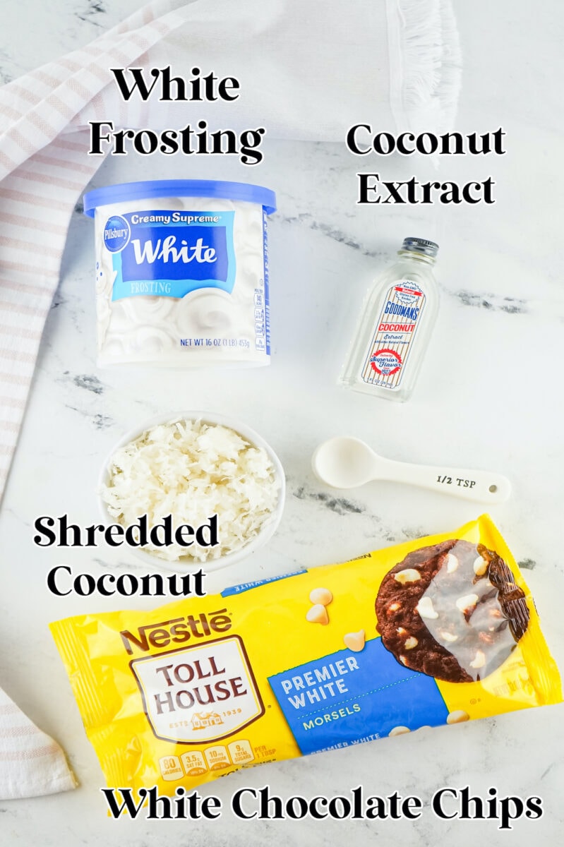 Ingredients for a delectable coconut fudge recipe: white frosting, coconut extract, shredded coconut, a 1/2 tsp measuring spoon, and a package of white chocolate chips on the countertop.