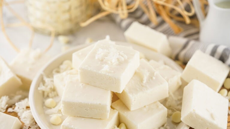 A plate of creamy white coconut fudge stacked with some shavings on top, surrounded by more shavings and partially visible decorations in the background.