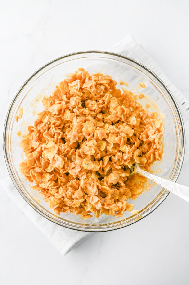 A clear bowl filled with cornflake clusters coated in a caramel-like mixture, placed on a white napkin.