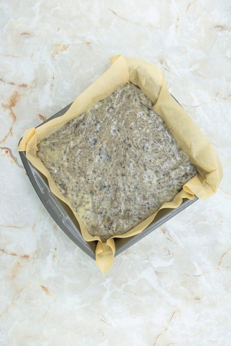 A baking tray lined with parchment paper containing unbaked chia seed bread dough on a marbled surface.