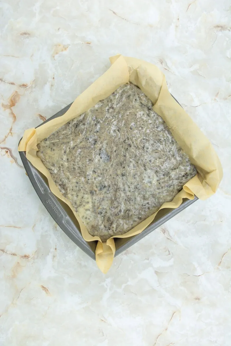 A baking tray lined with parchment paper containing unbaked chia seed bread dough on a marbled surface.