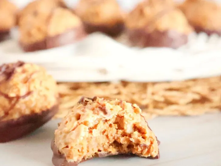 Close-up of a chocolate-coated cookie with a bite taken out, revealing a peanut butter filling. Other cookies are blurred in the background.