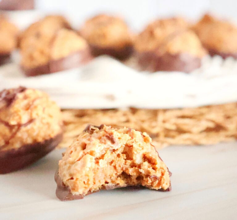 Close-up of a chocolate-coated cookie with a bite taken out, revealing a peanut butter filling. Other cookies are blurred in the background.