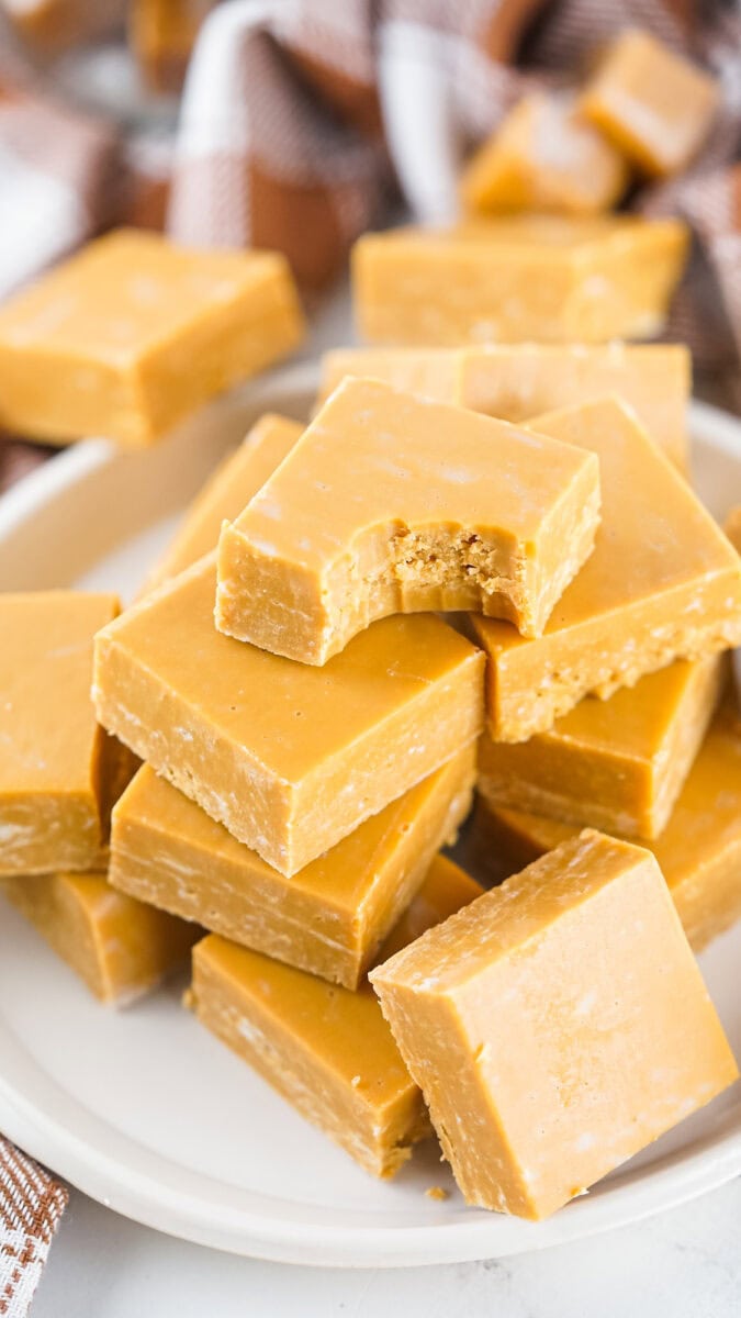 A plate of stacked peanut butter fudge squares, with one piece on top partially eaten.