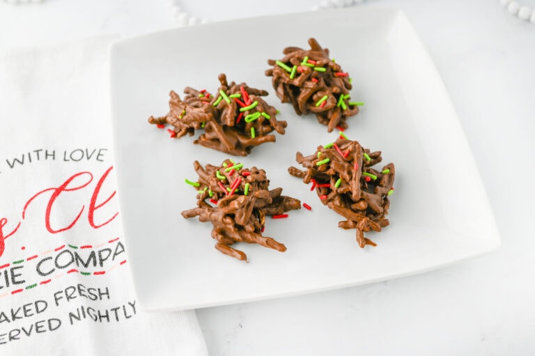 Four chocolate haystack cookies with red and green sprinkles on a white plate.