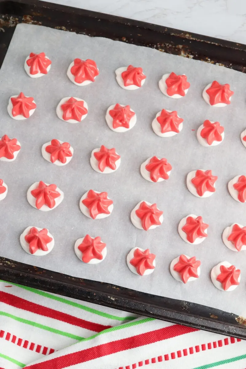 Rows of red and white meringue cookies on a parchment-lined baking tray, with a festive striped cloth beneath.