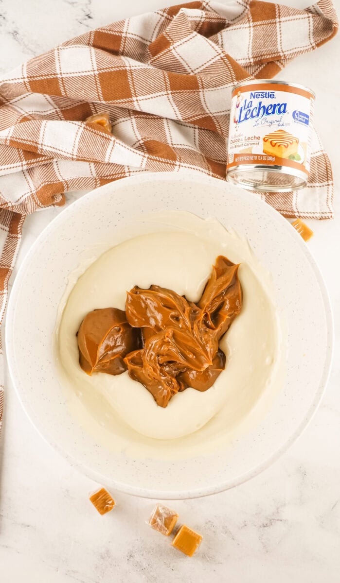 Bowl with melted white chocolate and dulce de leche, surrounded by a plaid cloth and a can of dulce de leche.