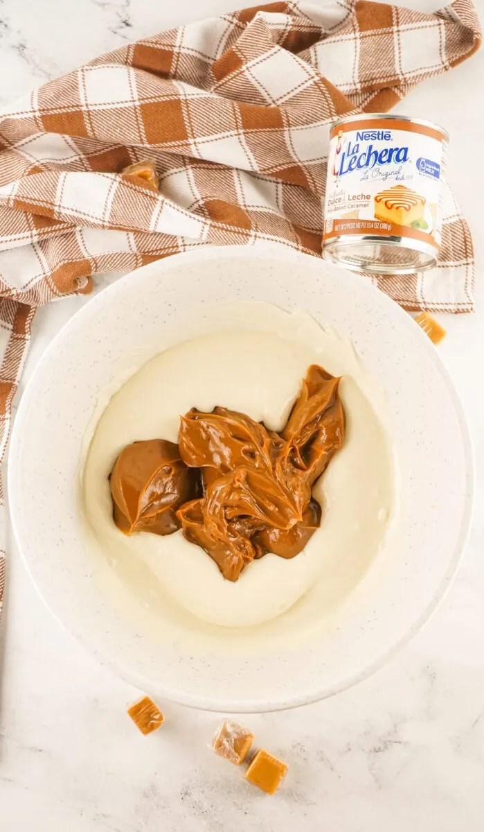 Bowl with melted white chocolate and dulce de leche, surrounded by a plaid cloth and a can of dulce de leche.