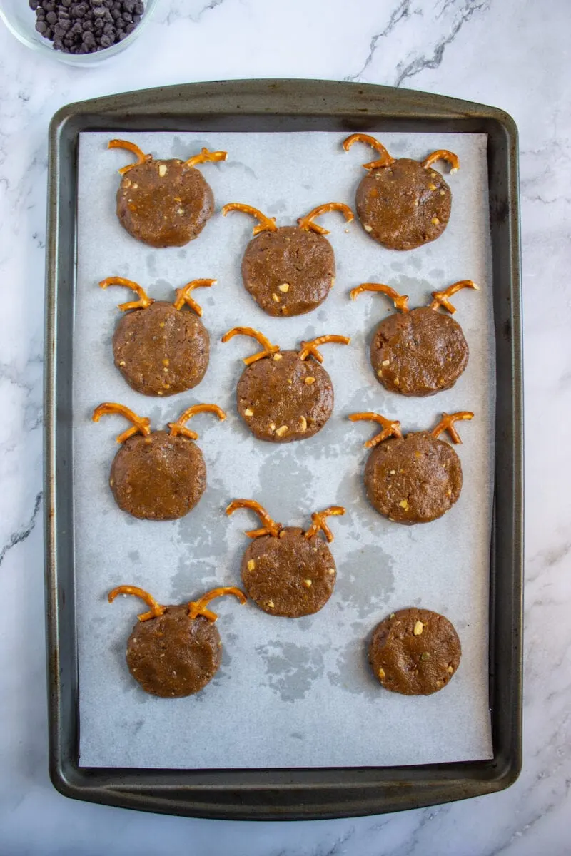 Cookie dough shaped like reindeer, with pretzel antlers, on a baking tray lined with parchment paper.