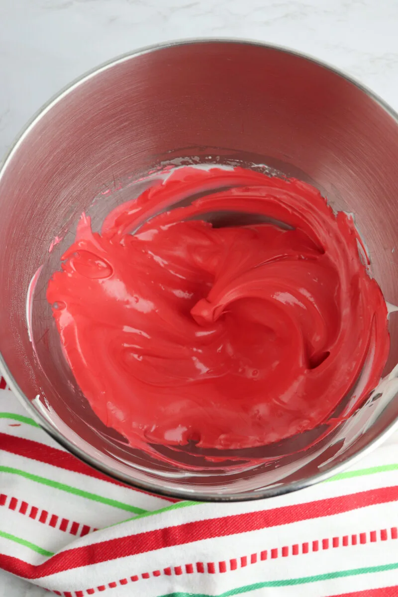 A metal mixing bowl with smooth red batter, placed on a striped red, green, and white cloth.