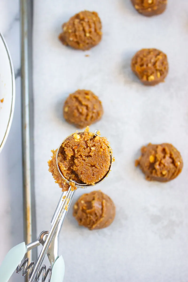 Cookie dough scooped onto a parchment-lined baking sheet, with a close-up of a scoop holding dough.