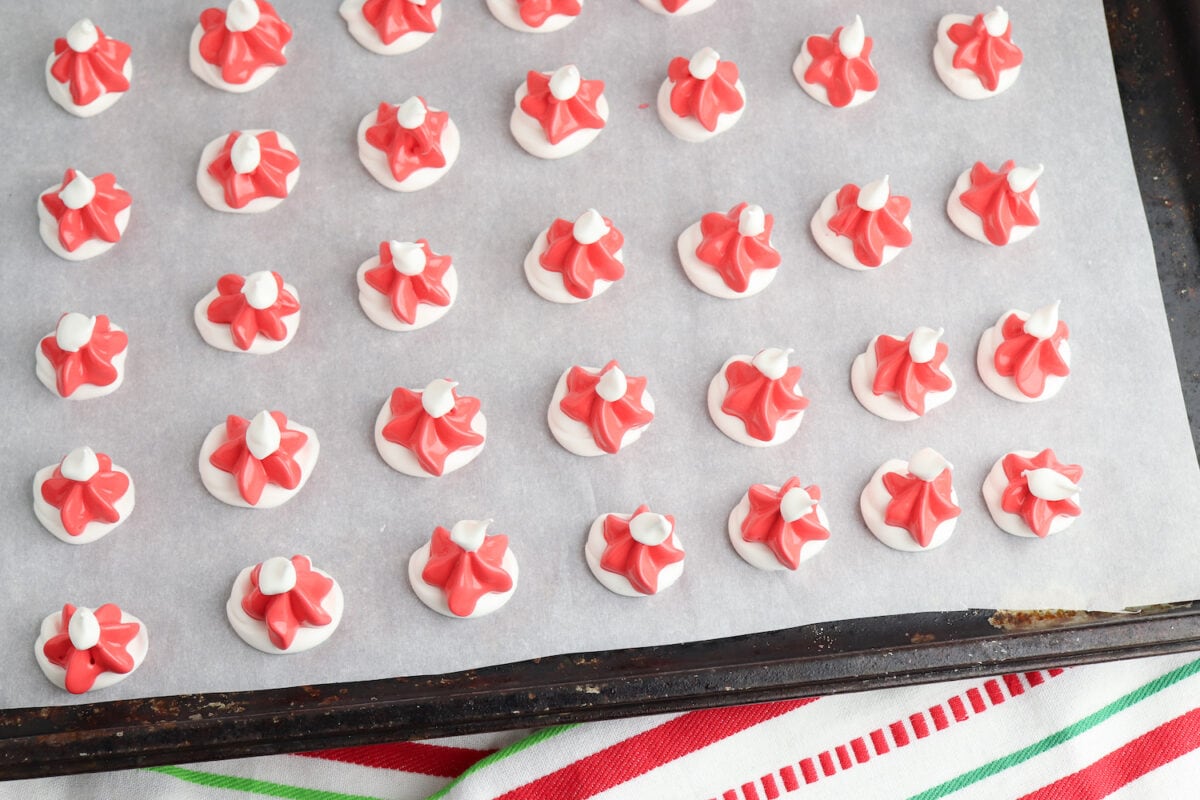 Red and white meringue cookies arranged in rows on a parchment-lined baking sheet.