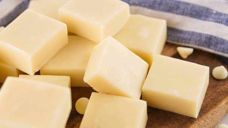 Several blocks of vanilla fudge and a few chocolate chips are arranged on a wooden surface with a striped cloth nearby.