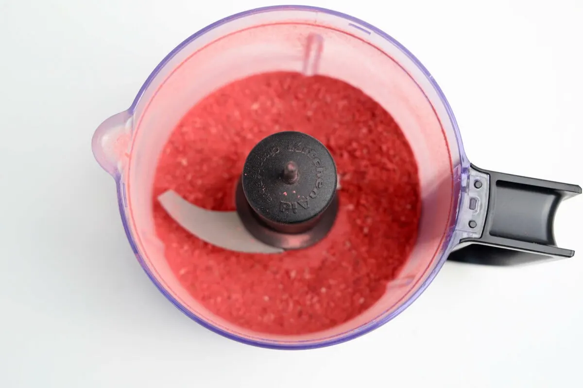 Top view of a food processor containing finely ground red powder with a visible blade, all set against a white surface.