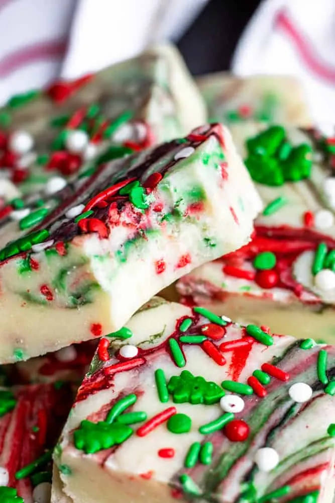 Christmas-themed fudge pieces with red, green, and white sprinkles and swirls, stacked together in a delightful display. Perfect for those exploring homemade fudge recipes this festive season.