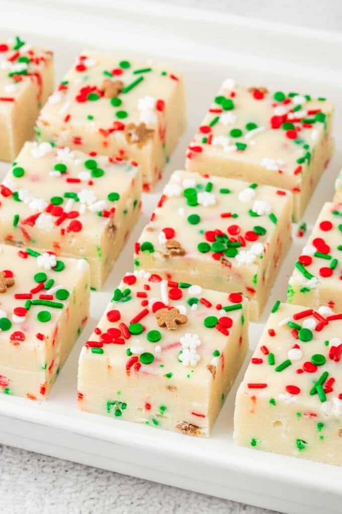 Squares of white fudge from our favorite homemade fudge recipes, topped with festive red, green, and white sprinkles, are neatly arranged on a pristine white tray.