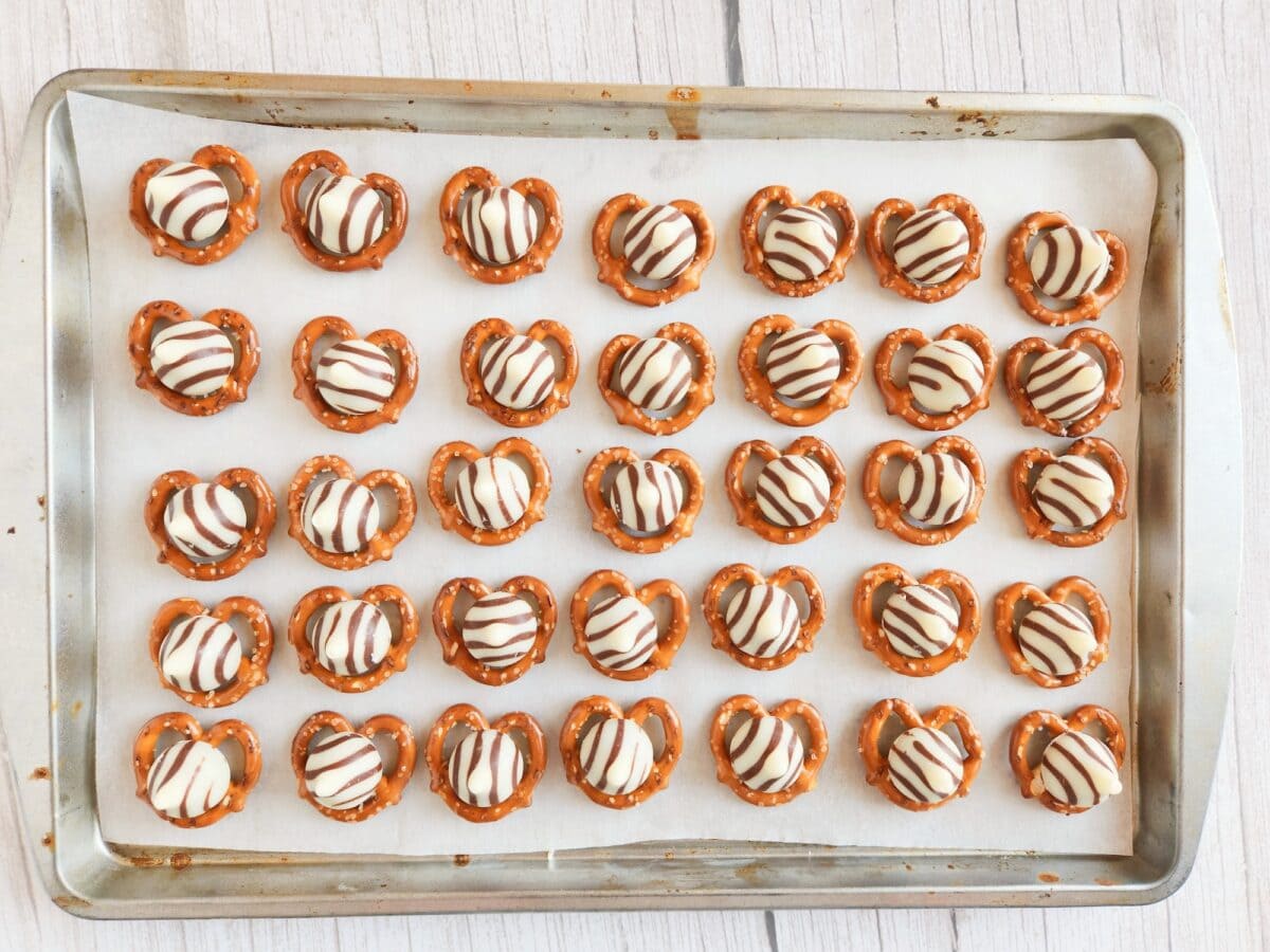 Baking tray with lined pretzels topped with white and dark chocolate stripes.