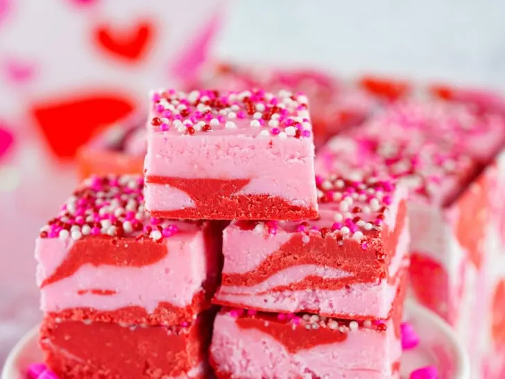 Square pieces of pink and red swirled Valentine Fudge, topped with colorful sprinkles, arranged on a plate.